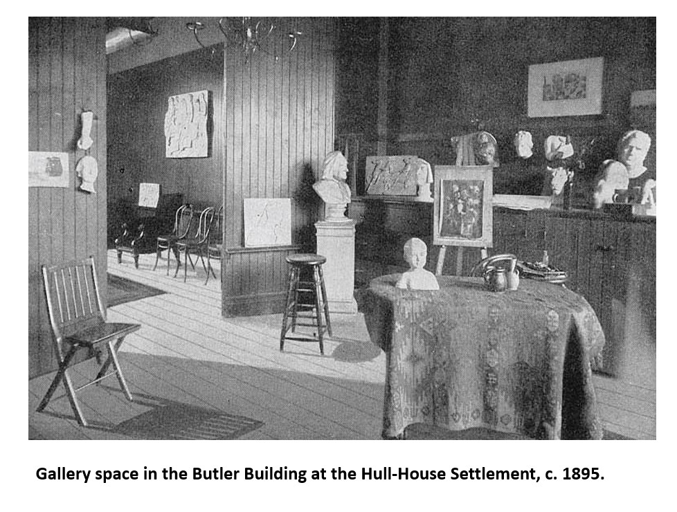 Black-and-white photo of an art gallery room with sculptures, paintings, wooden chairs, and a table at Hull-House Settlement, circa 1895.