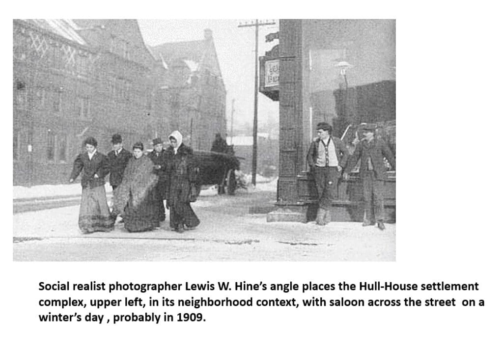 Historic black-and-white photo showing people walking on a snowy city street, with several buildings in the background, including the Hull-House settlement and a saloon. Likely taken in 1909 during winter.